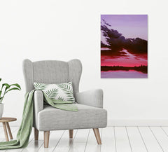 Gray armchair with a green blanket and leaf-patterned pillow, next to a wall with a colorful sunset landscape painting. Original fine art for sale.