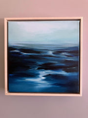 Framed abstract landscape ocean artwork with blue and black tones on a pink wall