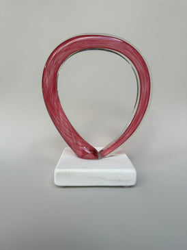 Pink glass sculpture abstract art with a white stone base against a gray background