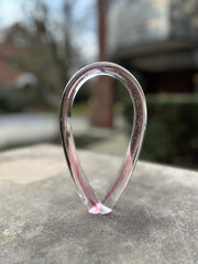An abstract glass sculpture with pink and clear hues, shaped in an arch or loop.