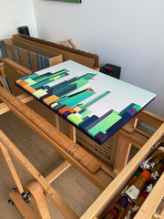 Colorful abstract painting on a table with an easel and art supplies in the background