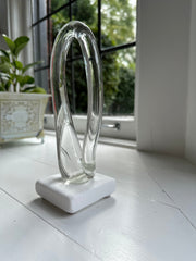 Clear glass contemporary sculpture by Pittsburgh based artist in front of a window and plant in the background