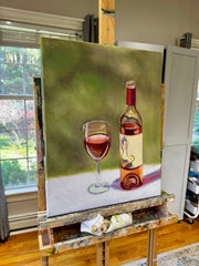 Painting of a wine bottle and glass on an easel indoors.