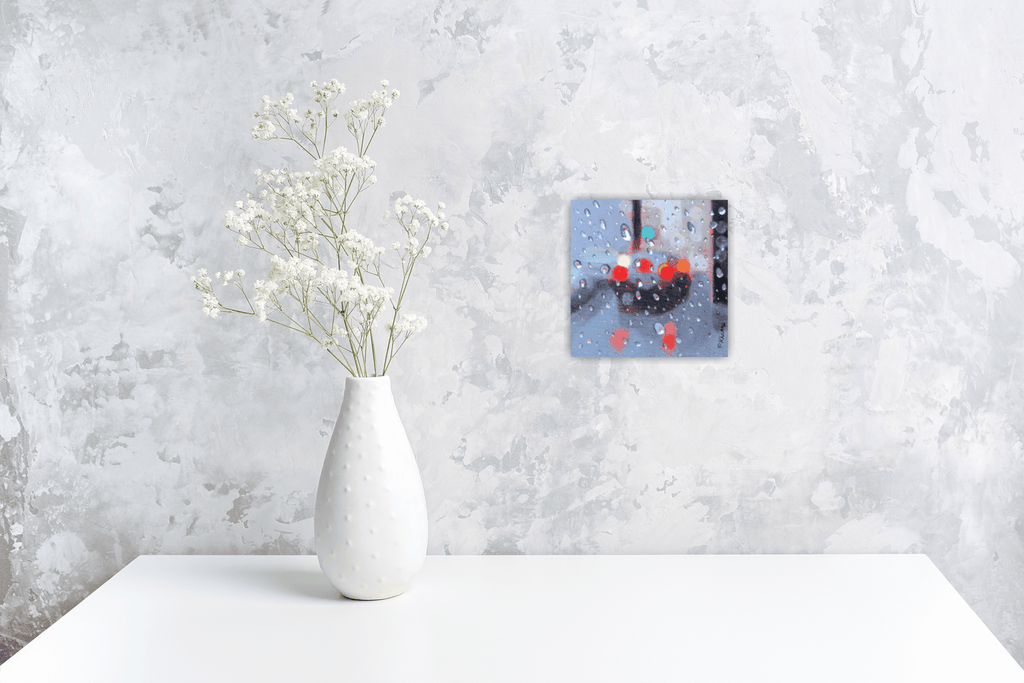 White vase with dried flowers on a white surface against a textured gray wall with small original painting.