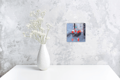 White vase with dried flowers on a white surface against a textured gray wall with small original painting.