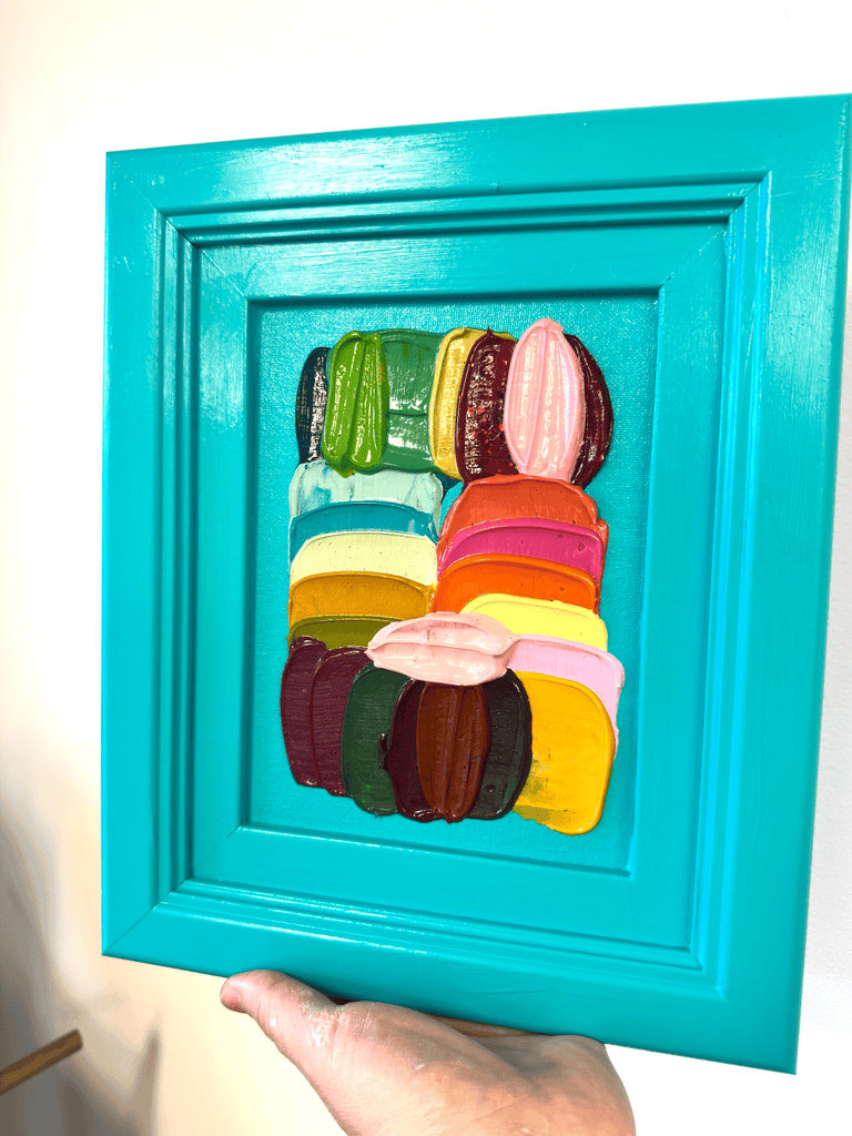 Colorful brushstrokes in a turquoise frame held by a hand.