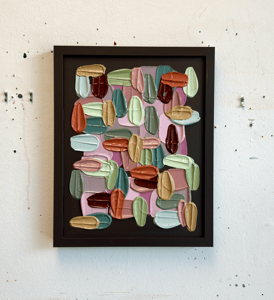Framed textured abstract art with colorful geometric shapes on a white wall.