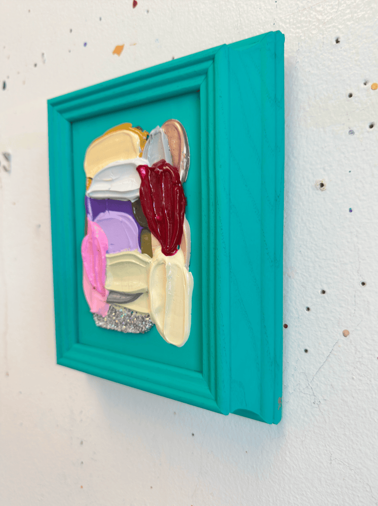 Colorful abstract art piece in a teal frame on a textured white wall