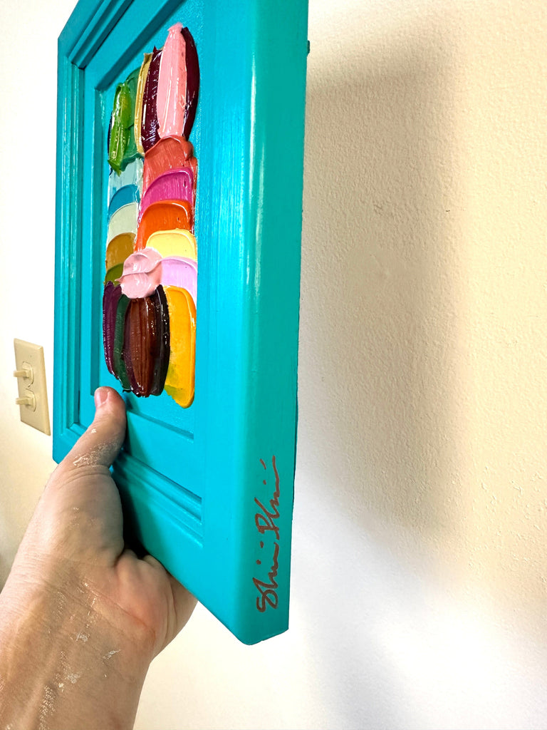 Turquoise frame with colorful brushtrokes held by a hand against a light background