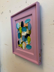 Colorful abstract art piece in a pink frame on a textured wall.