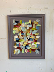 Framed abstract artwork with multicolored shapes on a textured wall.