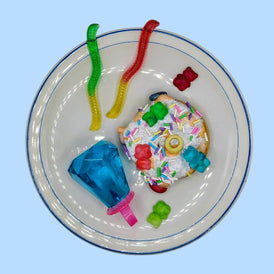 Colorful donut with sprinkles and gummy candies on a white plate against a light blue background, ceramic art