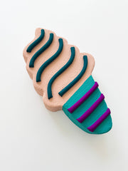 Ice cream cone wall sculpture with wavy patterns in teal, purple, and beige on a white background